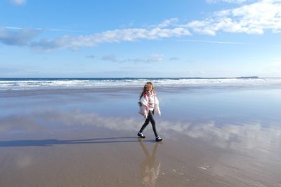 Side view of girl walking at beach against sky