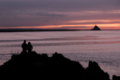 Silhouette rocks on beach against sky during sunset