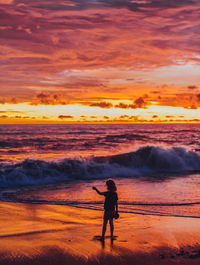 Boy standing at beach against sky during sunset