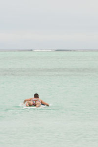 Rear view of young man lying on surfboard in sea