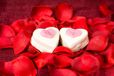 High angle view of heart shape desserts amidst rose petals on fabric