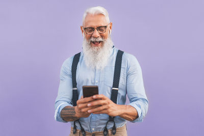 Bearded man using smart phone against purple background