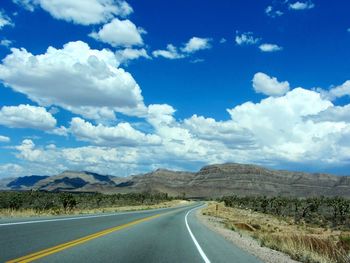 Empty road amidst landscape against blue sky