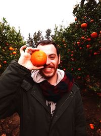 Portrait of young man holding orange while standing in orchard