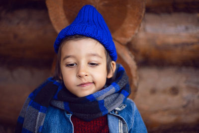 Boy child in a blue denim jacket and hat is sitting at a wooden house