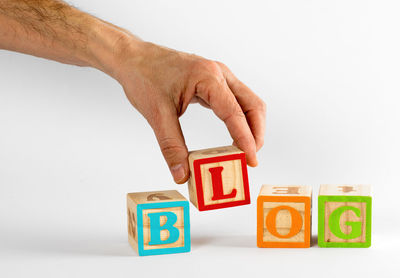 Cropped hand of man arranging toy blocks against white background