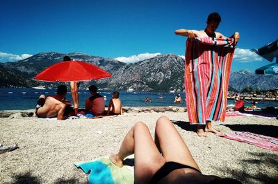 Low section of people relaxing on beach against clear blue sky