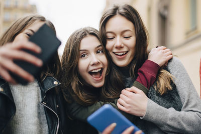 Girl taking selfie with female friends through mobile phone in city