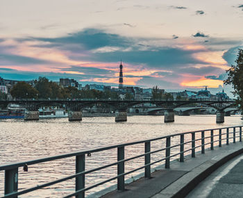 Bridge over river by buildings against sky during sunset