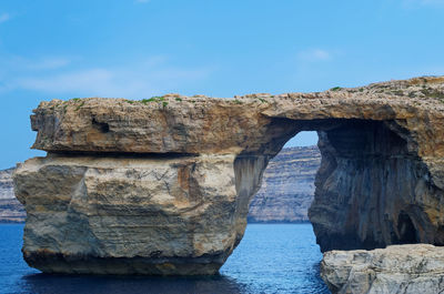 Rock formations by sea against blue sky