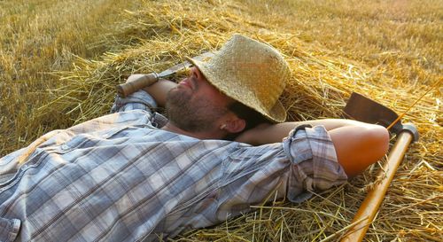 Farmer with work tool lying on hay at farm