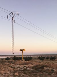 Electricity pylon on land against clear sky during sunset