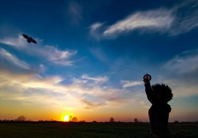 Silhouette kid flying kite in sky during sunset