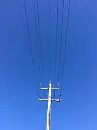 Low angle view of telephone pole against clear blue sky