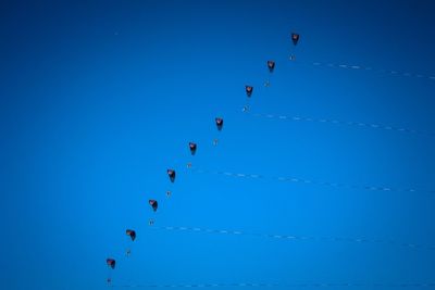 Low angle view of people paragliding against clear blue sky during sunny day