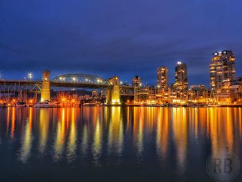 Illuminated buildings by sea against sky at night
