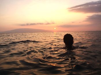 Silhouette person in sea against sky during sunset