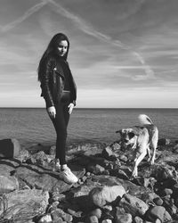 Full length of girl with dog on rock at beach against sky