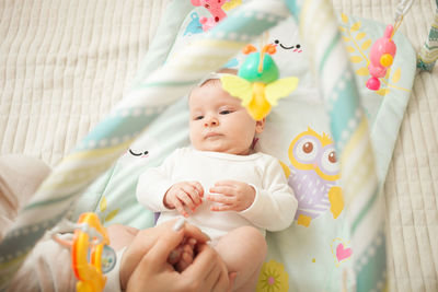 Child lies on bed, hanging toys, baby mat, newborn girl. developing, watching toys satisfied