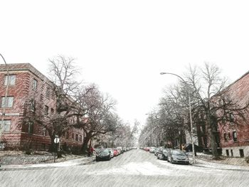 Cars on street by buildings against clear sky