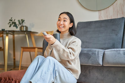 Young woman using mobile phone while sitting on sofa at home