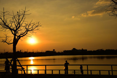 Silhouette people standing by lake against sky during sunset