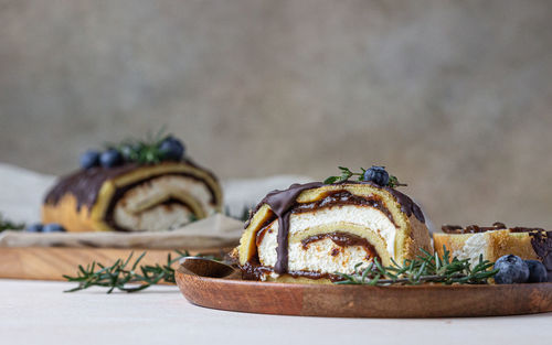 Sponge cake roll with chocolate and cream cheese with glaze, blueberry and rosemary.