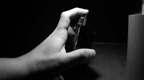 Cropped hand holding perfume bottle on table