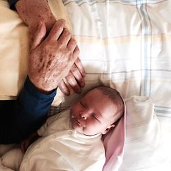 High angle view of person hands by baby sleeping on bed