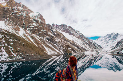 Rear view of young woman sitting by lake against mountain range