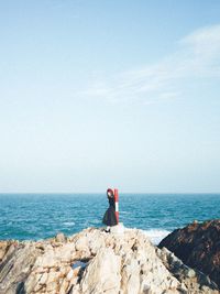 Rear view of man standing on rock by sea against clear sky