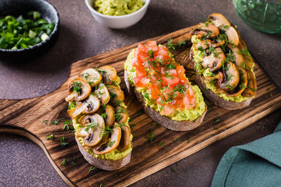 Sandwiches on rye bread with guacamole, fried mushrooms, tomatoes and dill on a board