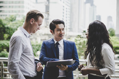 Business people discussing over file while standing outdoors