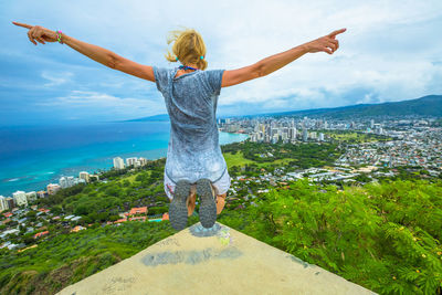 Rear view of woman with arms outstretched jumping against sea