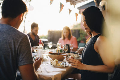 Woman using smart phone while sitting with friends at dining table in dinner party