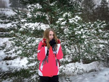 Young woman in winter clothes and pine trees covered in snow in the background