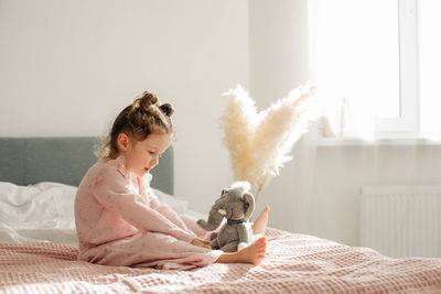 A cheerful little girl on the bed after waking up plays with her toy elephant