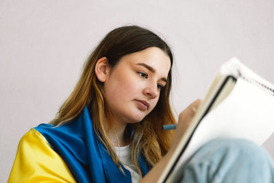 A ukrainian teenage girl is wrapped in the ukrainian flag and is drawing or doing homework