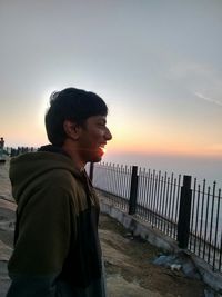 Side view of man looking at sea against sky during sunset