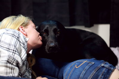 Young woman kissing black labrador on bed