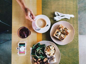 High angle view of cropped hand holding coffee cup by food served on table