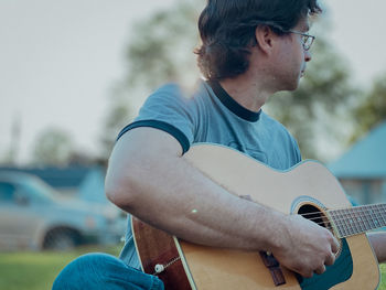 Midsection of young man playing acoustic  guitar on a summer evening