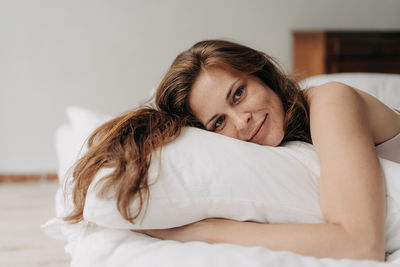 Beautiful natural authentic red-haired woman lies on a bed on a white bedclothes.