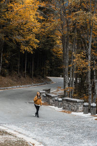 Young woman wearing winter clothes, walking on empty winding road in mountains in autumn