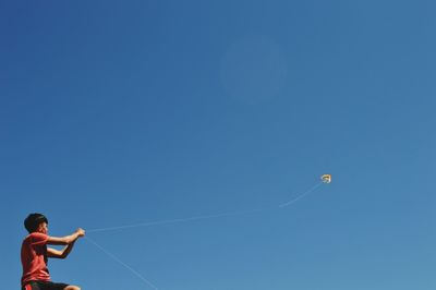 Low angle view of boy flying kite against clear blue sky