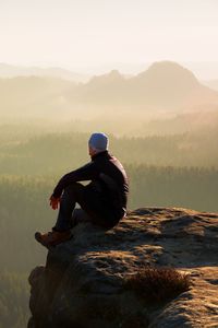 Man sitting on rock by mountain against sky