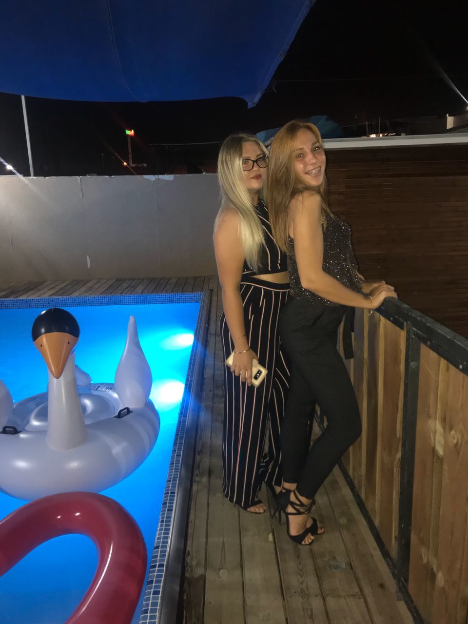 two people, real people, leisure activity, togetherness, lifestyles, young women, young adult, women, full length, railing, bonding, emotion, smiling, water, adult, standing, night, happiness, fashion, swimming pool, beautiful woman, hairstyle