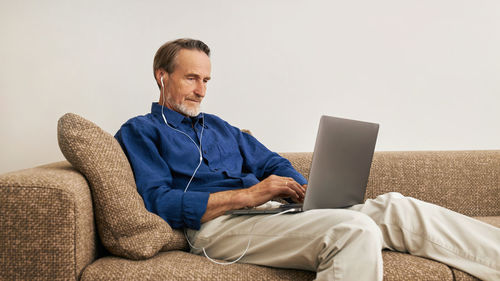 Senior man using laptop sitting on sofa at home