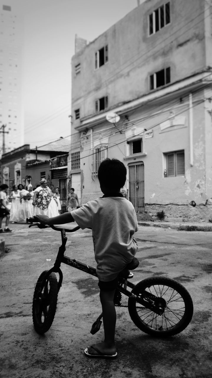 rear view, architecture, building exterior, built structure, full length, real people, transportation, one person, street, men, mode of transport, city, day, outdoors, sky, people