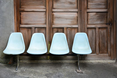 A row of old light blue plastic chairs on cement floor with wooden door background, lonely concept